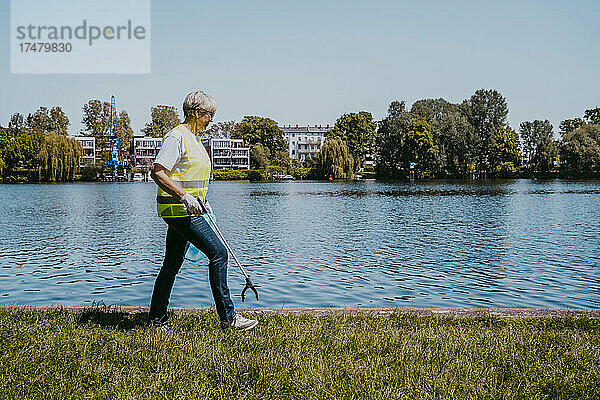 Ältere Klimaaktivistin geht an einem sonnigen Tag mit einer Klaue am See spazieren