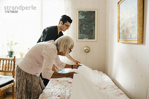 Ältere Frau und männlicher Pfleger legen Decke auf Bett zu Hause