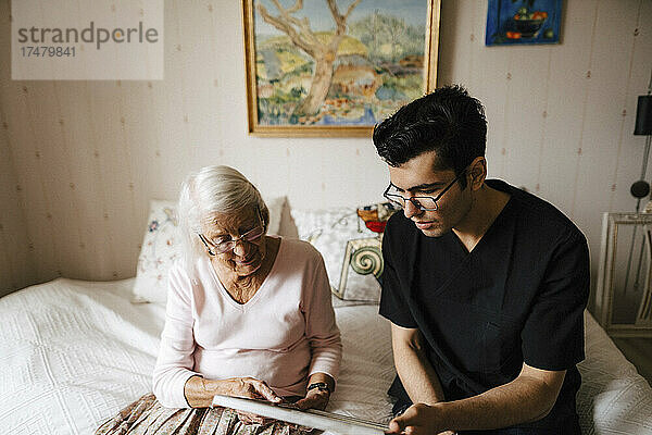 Junger Krankenpfleger zeigt einer älteren Frau  die zu Hause auf dem Bett sitzt  einen Spiegel