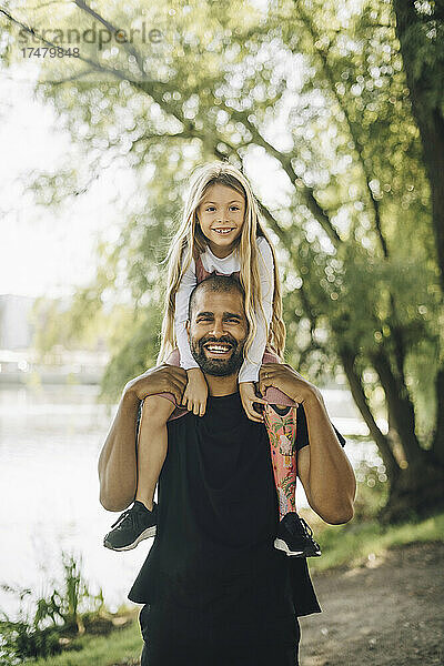 Porträt eines Vaters  der seine Tochter im Park auf der Schulter trägt