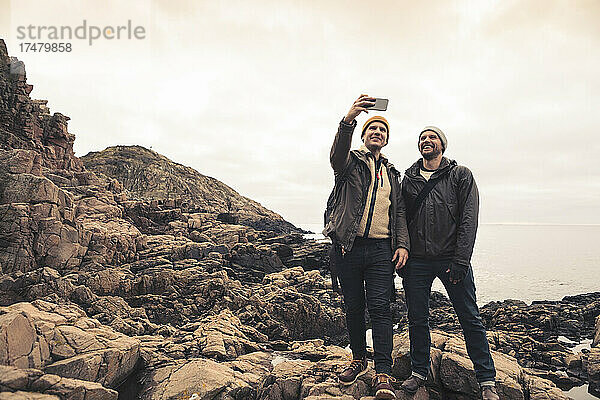 Männliche Freunde machen ein Selfie mit ihrem Smartphone  während sie am Strand stehen