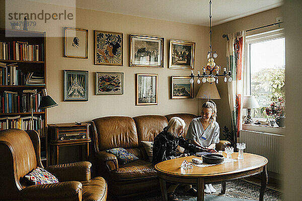 Weibliche Krankenschwester und ältere Frau unterhalten sich auf dem Sofa im Wohnzimmer sitzend