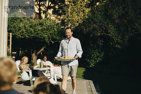 Lächelnder Vater mit Essen im Hinterhof während einer Gartenparty