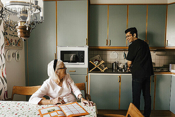 Ältere Frau im Gespräch mit männlichem Pflegepersonal bei der Arbeit in der Küche