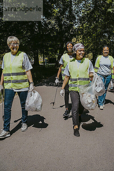 Multirassische weibliche Freiwillige mit Plastiktüten  die an einem sonnigen Tag im Park spazieren gehen