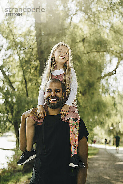 Fröhlicher Vater trägt behinderte Tochter auf den Schultern beim Spaziergang im Park
