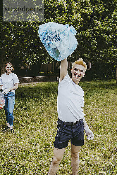 Fröhlicher männlicher Freiwilliger zeigt Plastiktüte beim Putzen im Park