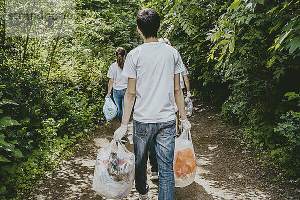 Rückansicht von männlichen und weiblichen Umweltschützern  die mit Plastiktüten durch einen Park gehen