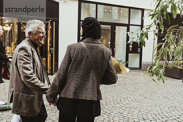 Glücklicher älterer Mann im Gespräch mit einer Frau beim Gehen auf der Straße in der Stadt