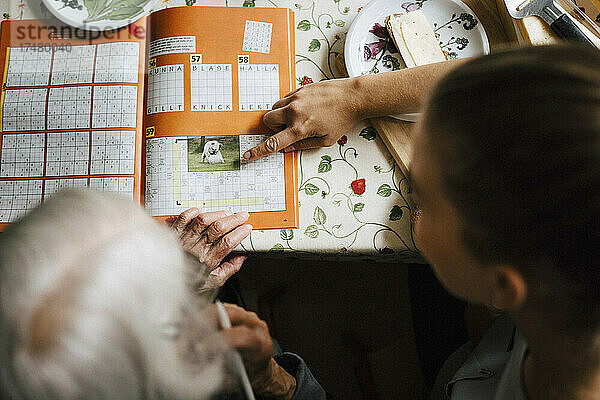 Hohe Winkel Ansicht der weiblichen Betreuer lösen Kreuzworträtsel mit älteren Frau am Tisch