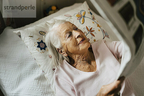 Hoher Blickwinkel auf eine ältere Frau  die auf dem Bett liegend Zeitung liest