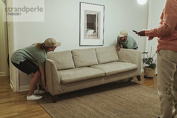 Männliche und weibliche Mitarbeiter tragen ein Sofa in das Wohnzimmer eines Kunden