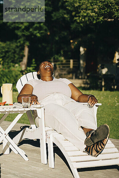 Mittlere erwachsene Frau lachend auf einem Liegestuhl sitzend während einer Gartenparty