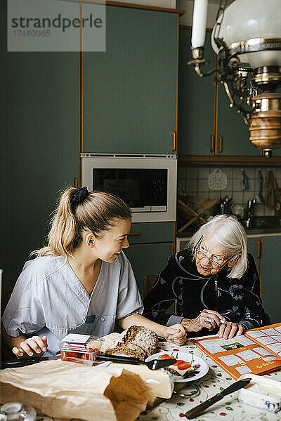 Lächelnde Krankenschwester unterrichtet ältere Frau am Esstisch in der Küche