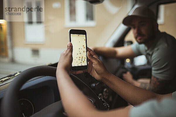 Beschnittenes Bild einer Zustellerin  die das Smartphone eines männlichen Mitarbeiters im Lieferwagen benutzt