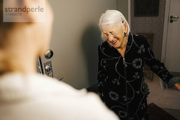 Ältere Frau lacht im Gespräch mit einer Krankenschwester zu Hause
