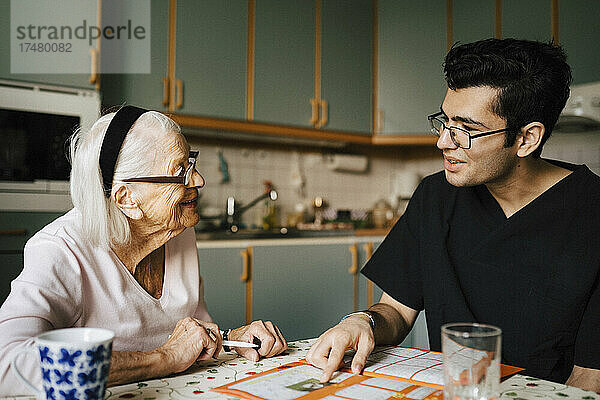 Lächelnde ältere Frau im Gespräch mit Pfleger in der Küche zu Hause