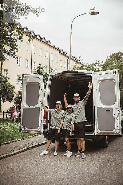 Fröhliche weibliche und männliche Mitarbeiter mit erhobenen Händen am Lieferwagen