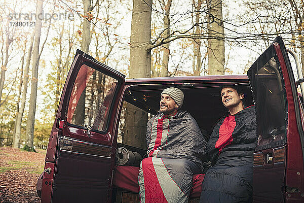 Lächelnde männliche Freunde unter Decken im Campingwagen sitzend