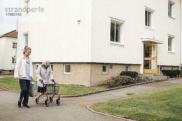 Weibliche Betreuerin geht mit einer älteren Frau durch ein Gebäude auf dem Fußweg