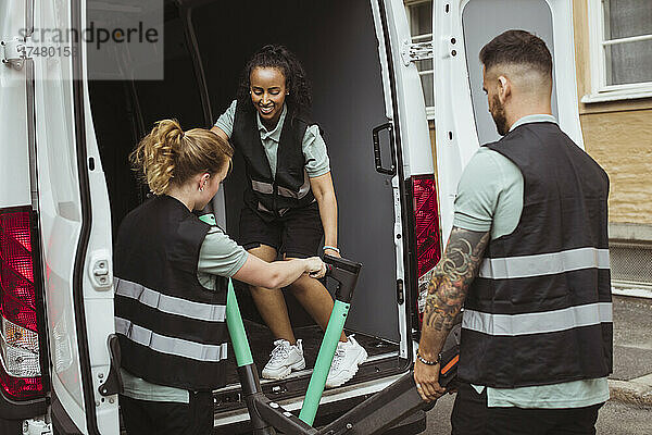 Eine Zustellerin hilft einem männlichen und einem weiblichen Mitarbeiter beim Einladen eines Elektrorollers in einen Lieferwagen