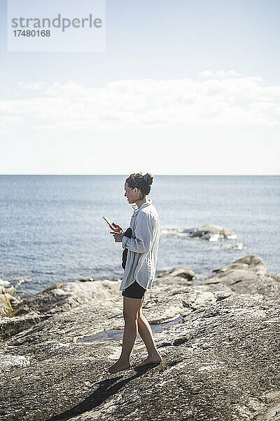 Seitenansicht einer Frau  die im Sommerurlaub auf einem Felsen am Meer spazieren geht