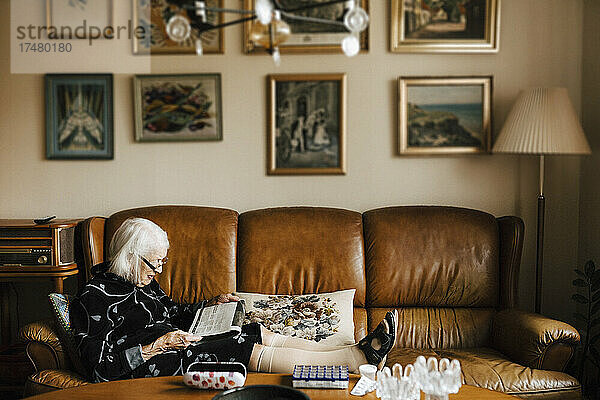 Ältere Frau liest Zeitung  während sie auf dem Sofa im Wohnzimmer sitzt