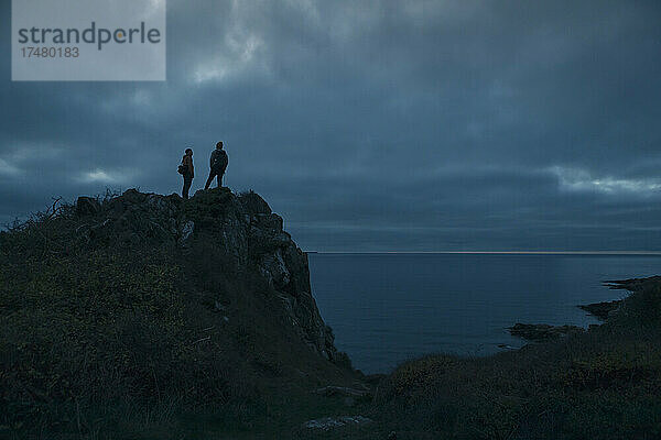 Ältere männliche Freunde stehen auf einem Hügel am Meer in der Abenddämmerung