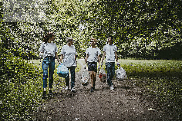 Weibliche und männliche Freiwillige unterhalten sich beim Spaziergang mit Plastiktüten im Park