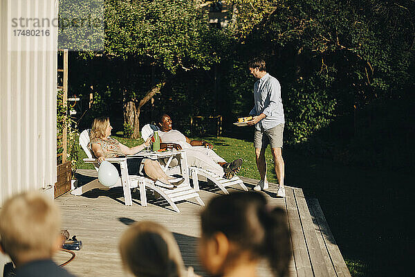 Mann serviert Frauen auf der Terrasse während einer Gartenparty Essen