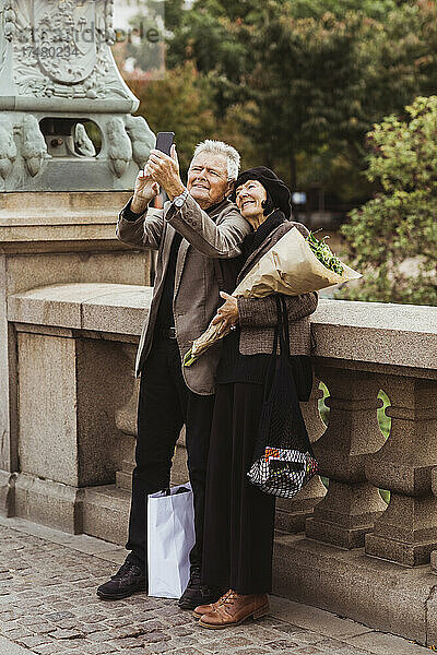 Glückliches älteres Paar  das ein Selfie mit seinem Smartphone macht  während es auf einer Brücke steht