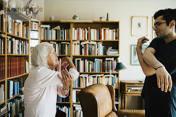 Männlicher Mitarbeiter im Gesundheitswesen hilft einer älteren Frau bei ihren Übungen zu Hause
