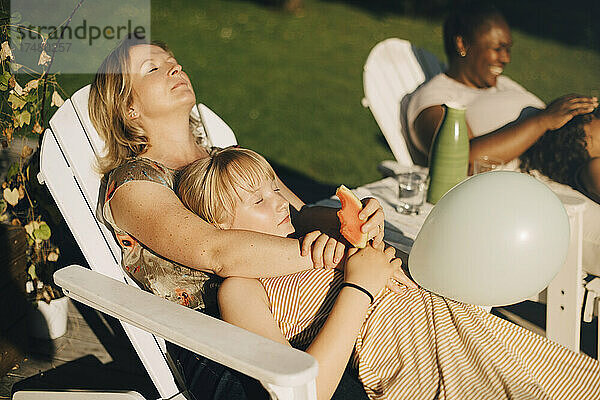 Mutter entspannt sich mit Tochter im Garten auf einem Liegestuhl an einem sonnigen Tag