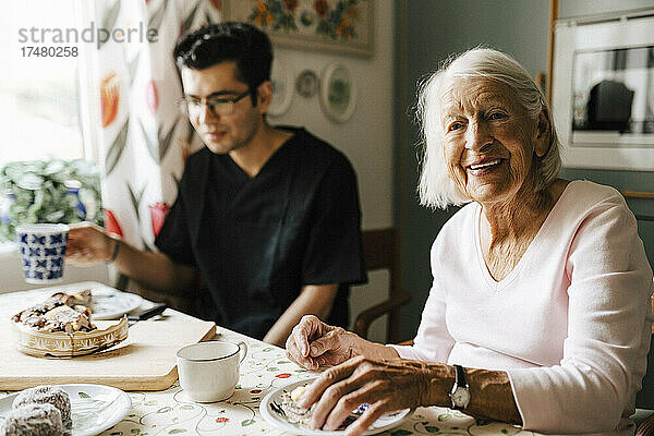 Porträt einer älteren Frau  die mit einem Pfleger in der Küche eines Hauses sitzt