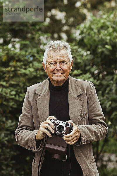Porträt eines älteren Mannes mit Kamera im Park