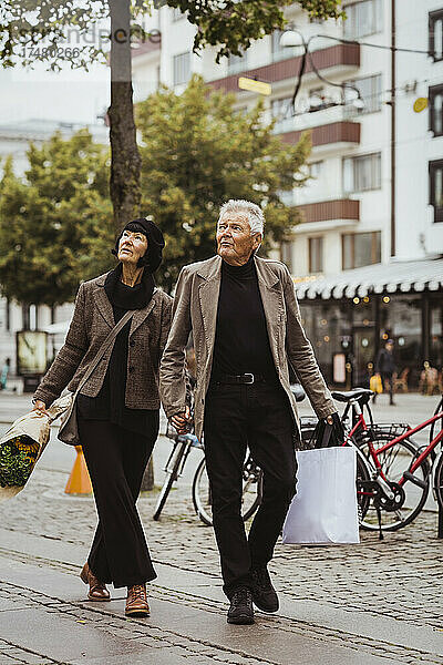Älteres Paar hält sich an den Händen  während es auf einem Fußweg in der Stadt spazieren geht