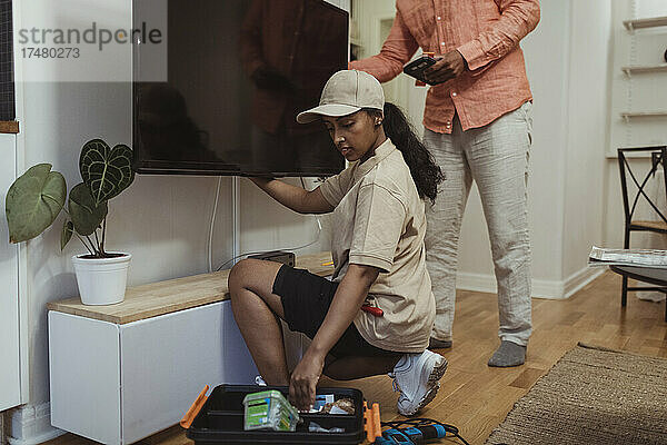 Ein weiblicher Techniker sieht sich die Geräte an  während er einen Fernseher zu Hause repariert