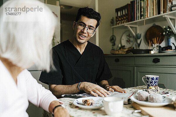 Lächelnder männlicher Pfleger im Gespräch mit einer älteren Frau in der Küche zu Hause