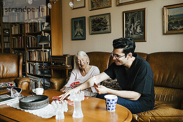 Ältere Frau und männliche Krankenschwester spielen Karten im Wohnzimmer zu Hause