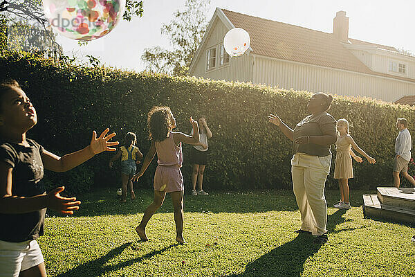 Frau und Kinder spielen mit Luftballons im Hinterhof an einem sonnigen Tag