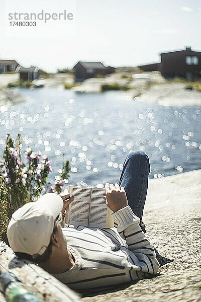 Mann liest ein Buch  während er an einem sonnigen Tag auf einem Felsen liegt