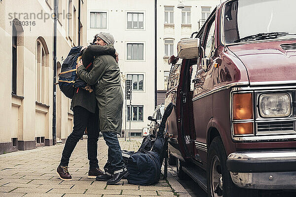 Seitenansicht von männlichen Freunden  die sich auf dem Fußweg neben einem Lieferwagen umarmen