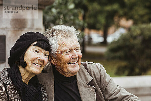 Fröhliches älteres Paar  das im Park sitzt und wegschaut