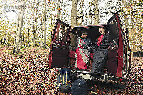 Mann  eingewickelt in eine Decke  gähnt mit einem Freund beim Zelten im Wald