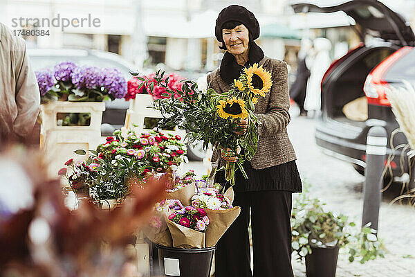 Lächelnde ältere Frau kauft Blumen auf dem Markt