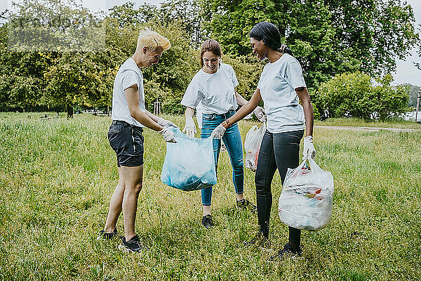 Fröhliche männliche und weibliche Freiwillige bei der Untersuchung von Plastikmüll im Park