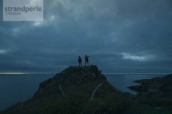 Männer auf dem Gipfel eines Hügels gegen den bewölkten Himmel in der Abenddämmerung