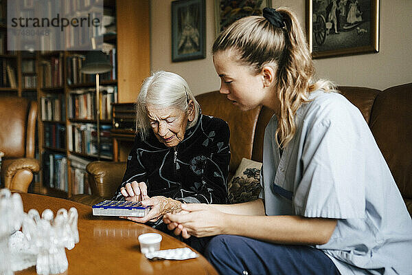 Ältere Frau unterhält sich mit einer weiblichen Betreuerin über einer Hausapotheke im Wohnzimmer
