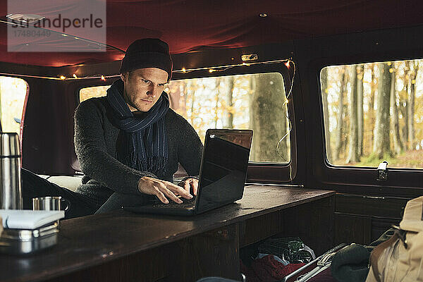 Männlicher Freiberufler arbeitet am Laptop im Campingbus