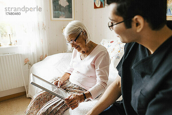 Ältere Frau schaut in den Spiegel  während sie bei einem männlichen Pfleger im Schlafzimmer sitzt